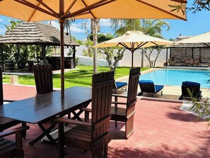 Un área junto a la piscina con mobiliario de madera, sombrillas y una vista despejada del agua.