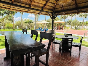 Un patio al aire libre con mesas, sillas, piscina y sombrillas.