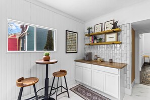 A kitchen with white cabinets, a wooden countertop, a coffee machine, and a small table with stools.