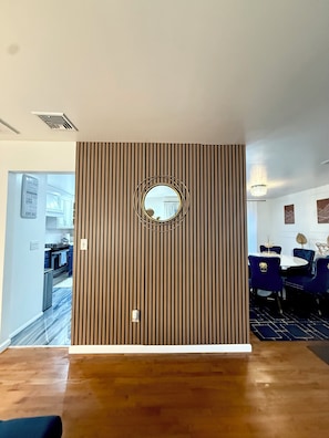 A room with a wooden slat wall, a round mirror, a chandelier, and a dining area with blue upholstered chairs. - TH Luxe Home, Sleeps 9, Your vacation home. 50 mint from NYC, attractions & more (Harriman)