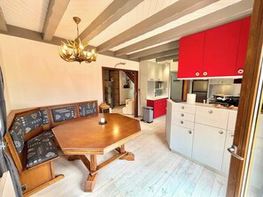 Een eetruimte met een houten tafel en banken, een kroonluchter, en een keuken met rode keukenkastjes.