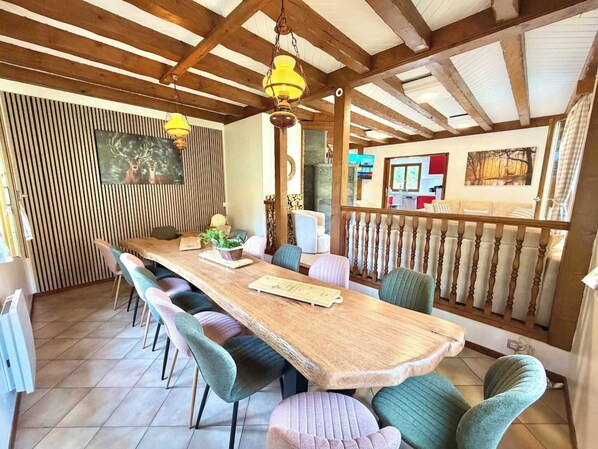 Een eethoek met een lange houten tafel, comfortabele stoelen en hangende hanglampen.