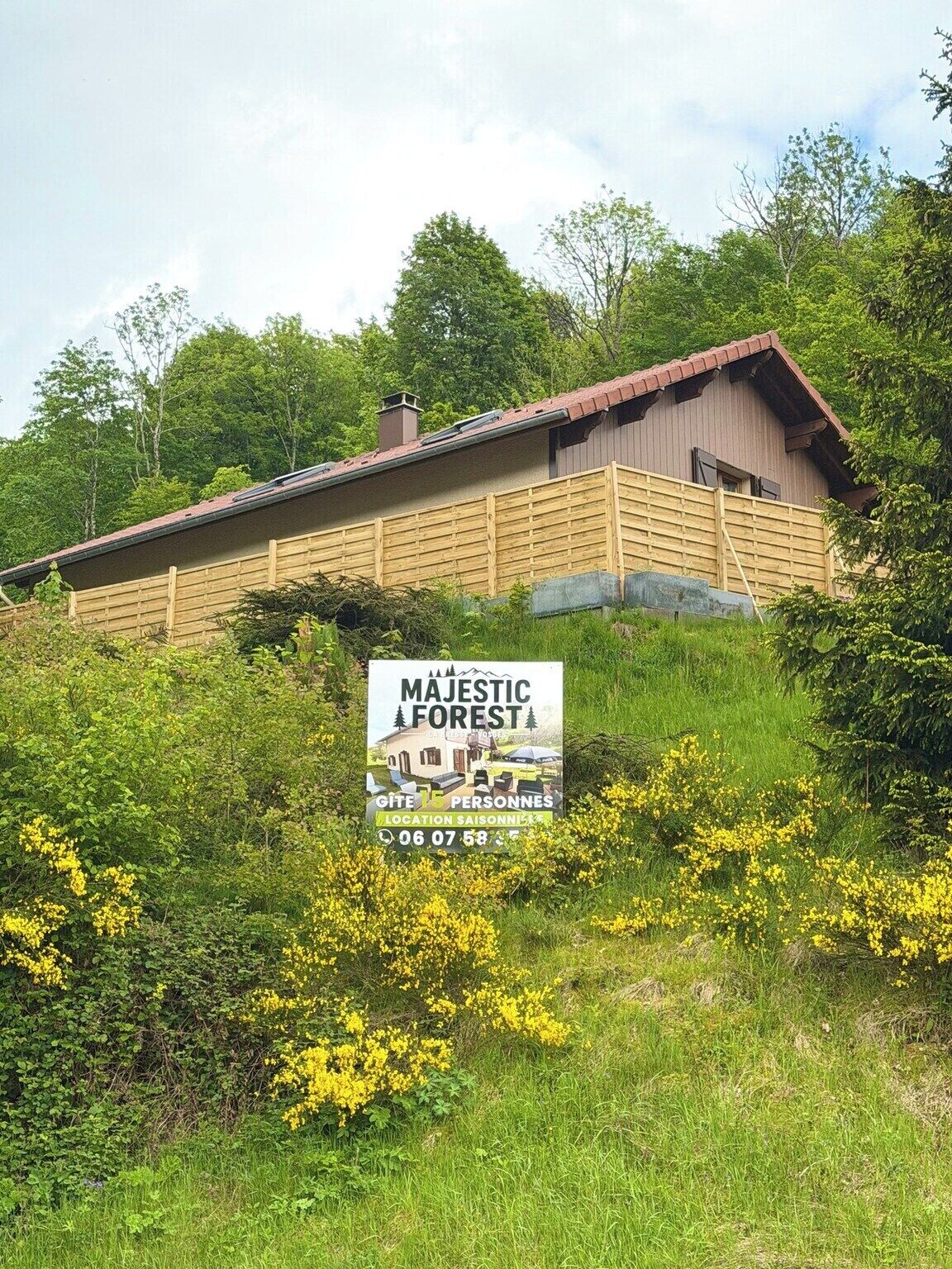A rustic wooden cabin with a red roof, surrounded by lush greenery and yellow flowers.