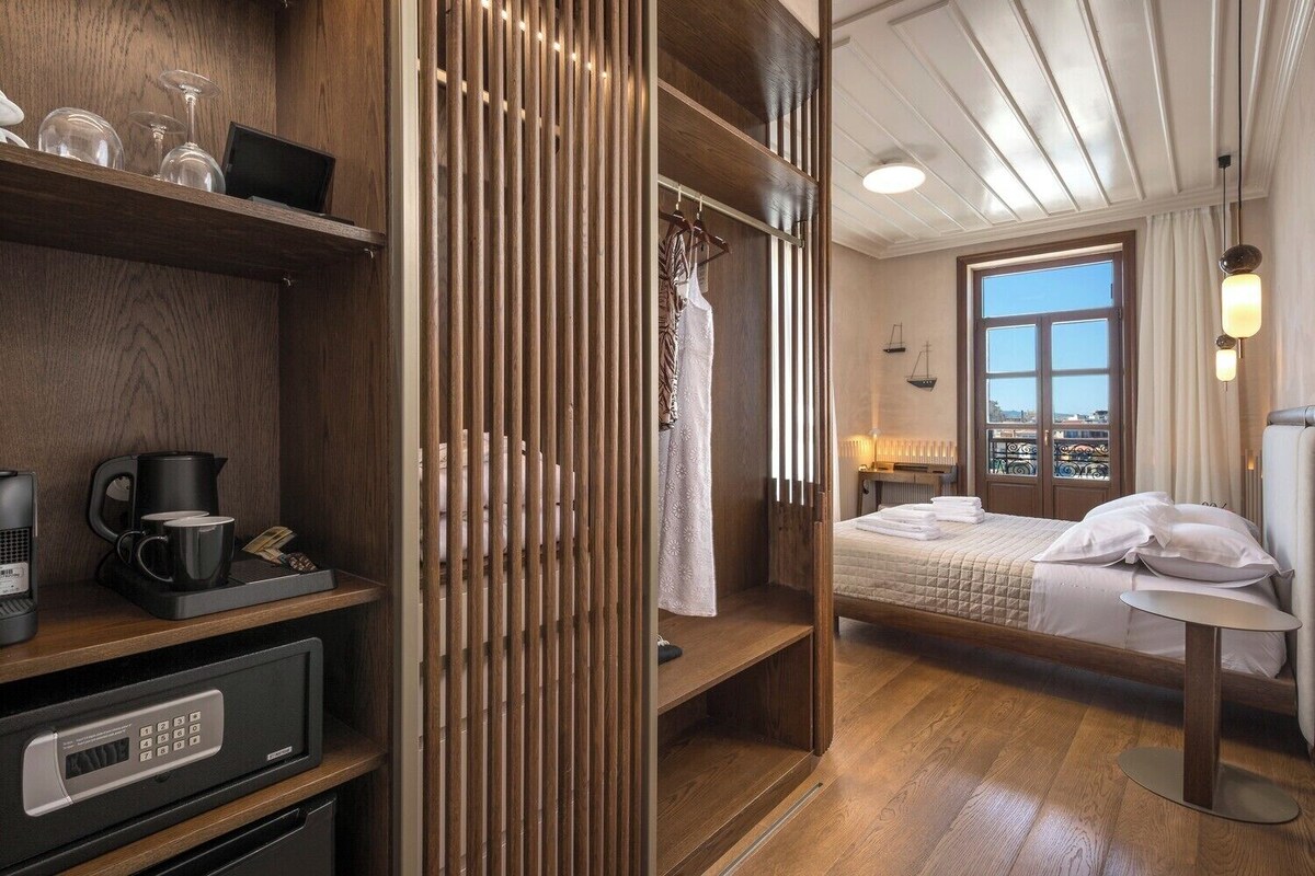 Quarto de hotel com cama, escrivaninha, cafeteira e vista para a cidade.