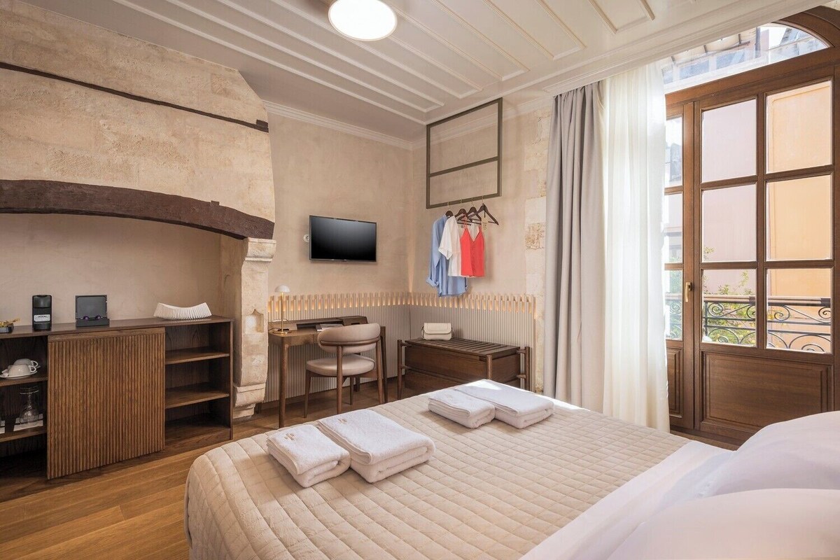 Quarto de hotel com cama, escrivaninha, cadeira, televisão e janela com cortinas.