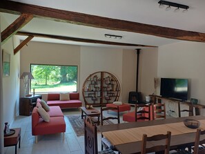 A living room with a red sofa, a wooden dining table, a TV, and a bookshelf. - Gîte le Bergerayre 6 people Swimming pool/Campagne 4-star accommodation (ST GRIEDE)