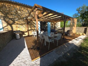 A covered outdoor patio with a stone wall, a grill, and a table with chairs. - Gîte le Bergerayre 6 people Swimming pool/Campagne 4-star accommodation (ST GRIEDE)