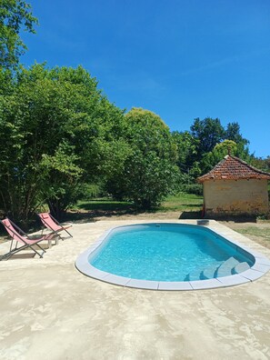 Ein Swimmingpool mit Liegestühlen, umgeben von Bäumen und einem kleinen Gebäude.