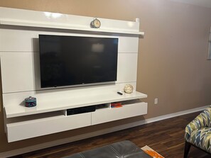 A living room with a flat-screen TV mounted on a white entertainment unit, a small decorative clock, and a remote control on the unit. - Entire townhouse in New Orleans, Louisiana. (New Orleans)