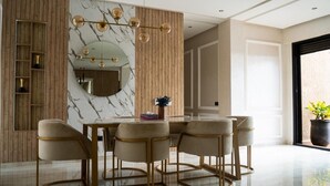 Un comedor moderno con pared de mármol, paneles de madera y una mesa de vidrio con cuatro sillas.