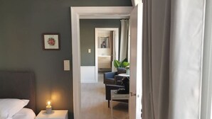 A bedroom with a bed, bedside table, chair, and a view into another room. - Spacious Quadruple Room w. Private Bathroom (Brugge)