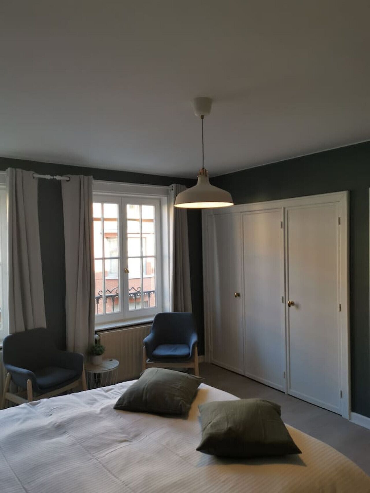 A bedroom with a bed, two chairs, a window, and a wardrobe.