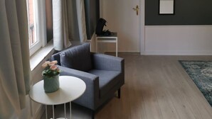 A modern living room with a grey sofa, a small round table, and a potted plant. - Spacious Quadruple Room w. Private Bathroom (Brugge)