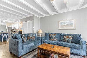 Ein Wohnzimmer mit zwei blauen Sofas, einem Holztisch und einer Küche im Hintergrund.