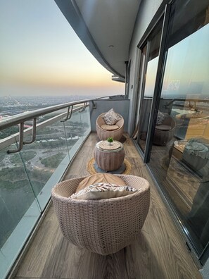 Un balcone con mobili in vimini, ringhiera in vetro e vista sulla città.
