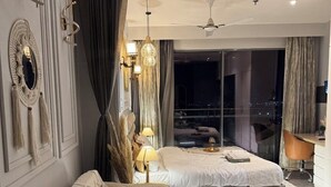 Une chambre d’hôtel moderne, dotée d’un canapé, d’une table basse, d’une lampe et offrant une vue sur la ville la nuit.