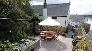 A patio with a wooden table and chairs, surrounded by potted plants and a small garden area. - Trelake Cottage (Tintagel)