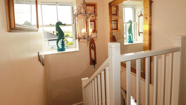 A staircase with a white railing, a chandelier, and a mirror on the wall. - Trelake Cottage (Tintagel)
