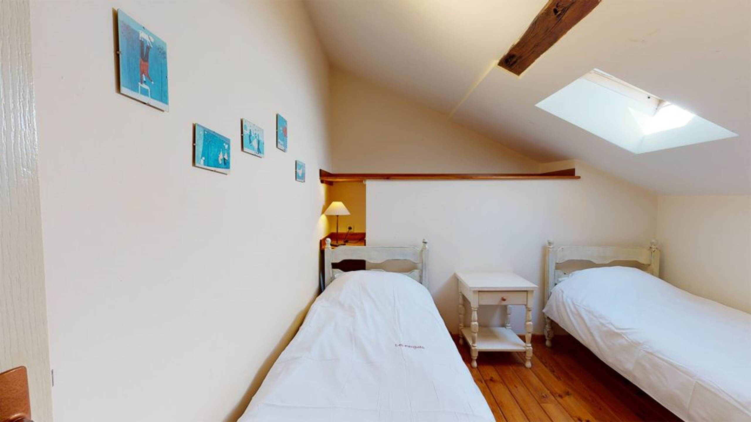 Una habitación pequeña y acogedora con dos camas, un escritorio y un tragaluz.