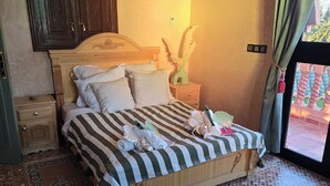 A bedroom with a wooden bed, a nightstand, a wall-mounted air conditioner, and a patterned floor. - Villa Gan Atlas - Luxury, pool, 7 suites, 14 pers. quiet & nature Marrakech (Marrakech)