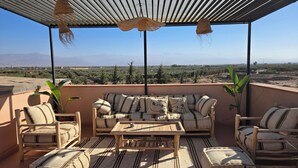 A covered outdoor seating area with a sofa, chairs, and a table, overlooking a landscape with trees and distant mountains. - Villa Gan Atlas - Luxury, pool, 7 suites, 14 pers. quiet & nature Marrakech (Marrakech)