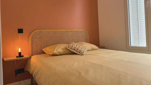 Une chambre à coucher avec un lit, une lampe de chevet et une fenêtre avec des stores.