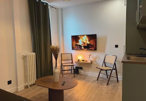 A modern living room with a fireplace, a dining table, two chairs, and a kitchen area. - Le vert Boulogne  (Boulogne-Billancourt)