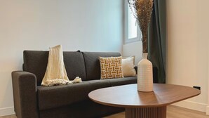 Un salon moderne avec un canapé marron foncé, une table basse ronde en bois et un vase contenant des fleurs séchées.