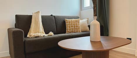 A modern living room with a dark brown sofa, a round wooden coffee table, and a vase with dried flowers.