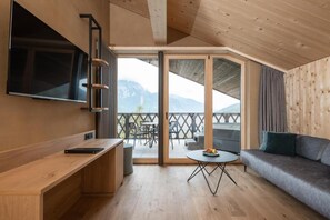 Une chambre moderne avec un plafond en bois, un téléviseur à écran plat fixé au mur, un canapé, une petite table ronde et un balcon avec un espace salon extérieur.