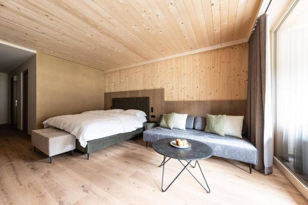 Un dormitorio moderno con cama, sofá, una mesita redonda y techo de madera.