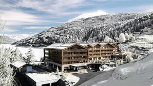 A multi-story building with a wooden facade, a ski lift, and a mountainous backdrop. - Das Gerstl Family Retreat (Curon Venosta)