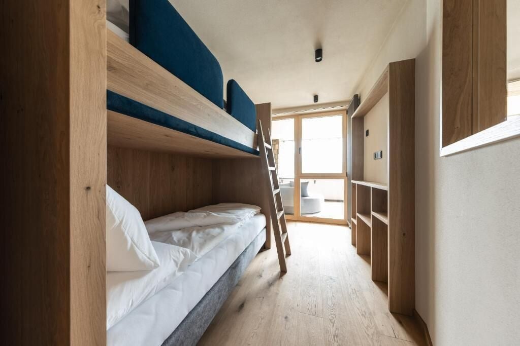 A bunk bed room with a ladder, wooden walls, and a window.