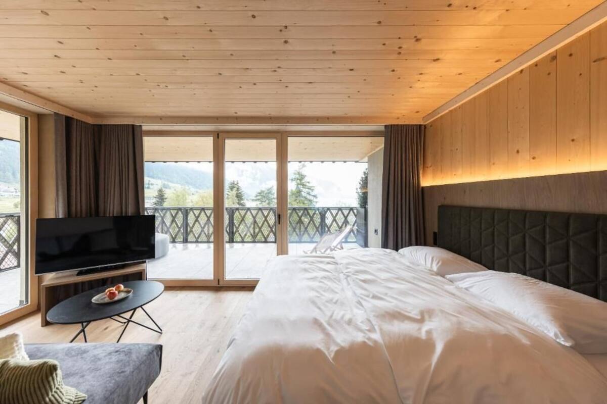 Un dormitorio con cama, televisor, una mesita y un balcón con vistas a las montañas.