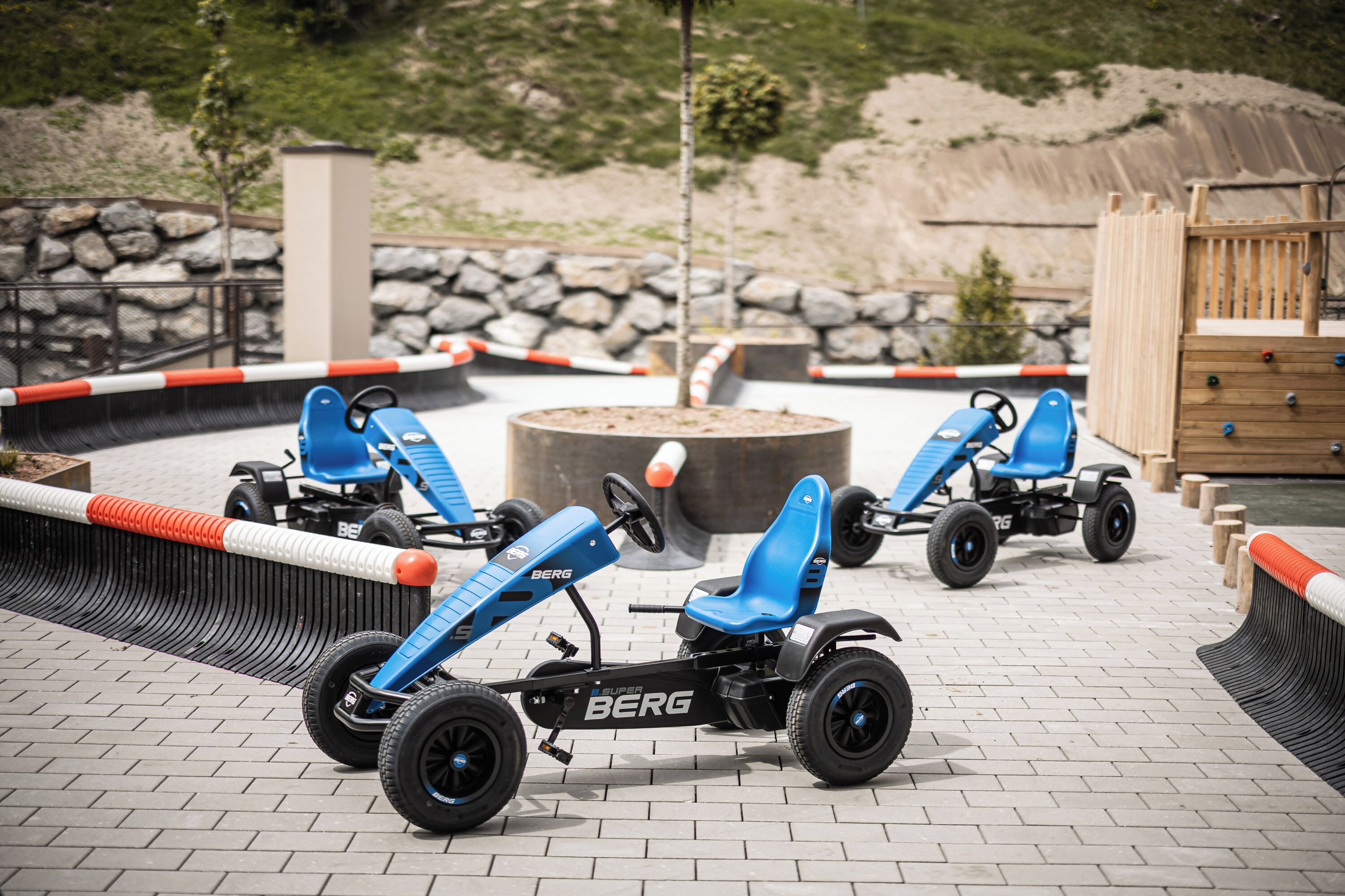 Go-karts on a paved area with a stone wall and wooden fence in the background.