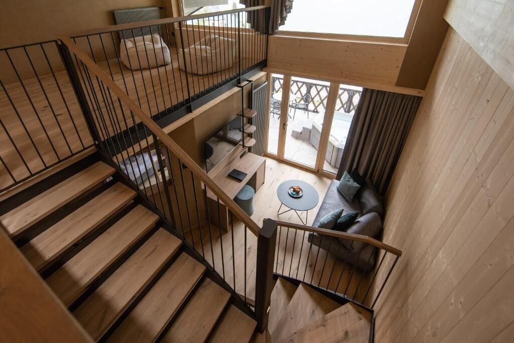 A multi-level wooden interior with a staircase, a seating area with a round table, and a view through a glass door.