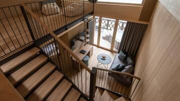 A multi-level wooden interior with a staircase, a seating area with a round table, and a view through a glass door.