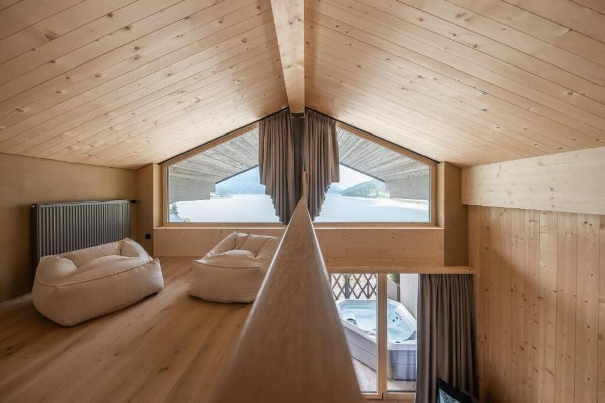 Una habitación con techos altos, vigas de madera, un ventanal grande y una bañera de hidromasaje visible a través del ventanal.