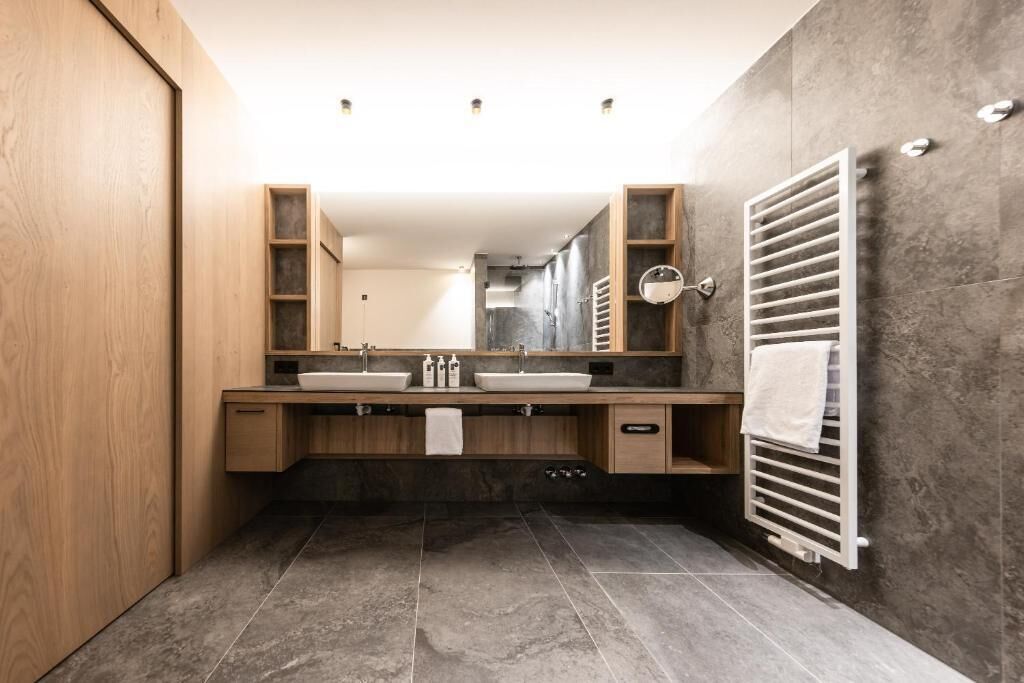 Un baño moderno con tocador de madera, dos lavamanos, un espejo grande y un perchero para toallas.