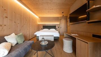 Une chambre d’hôtel moderne avec un plafond en bois, un lit recouvert de draps blancs, un canapé gris, une petite table ronde avec un plateau, et une armoire en bois.