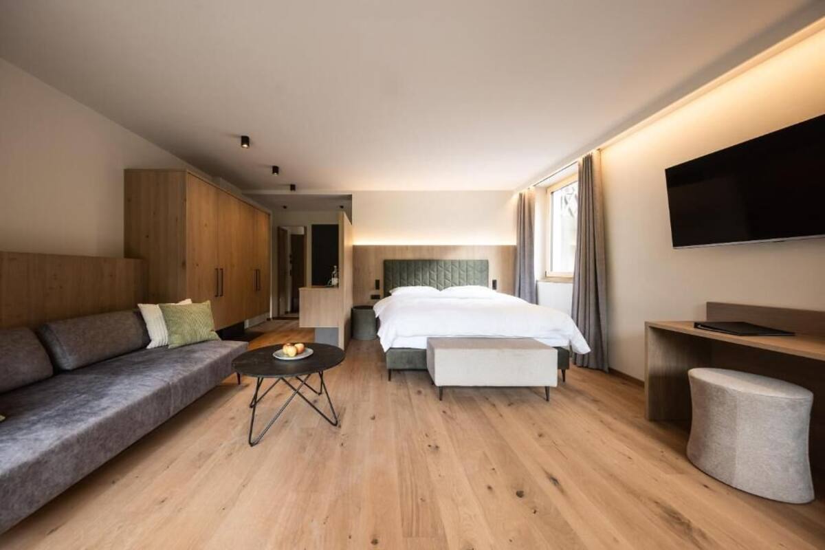 Una habitación de hotel moderna con cama, sofá, mesita de noche y televisión en la pared.