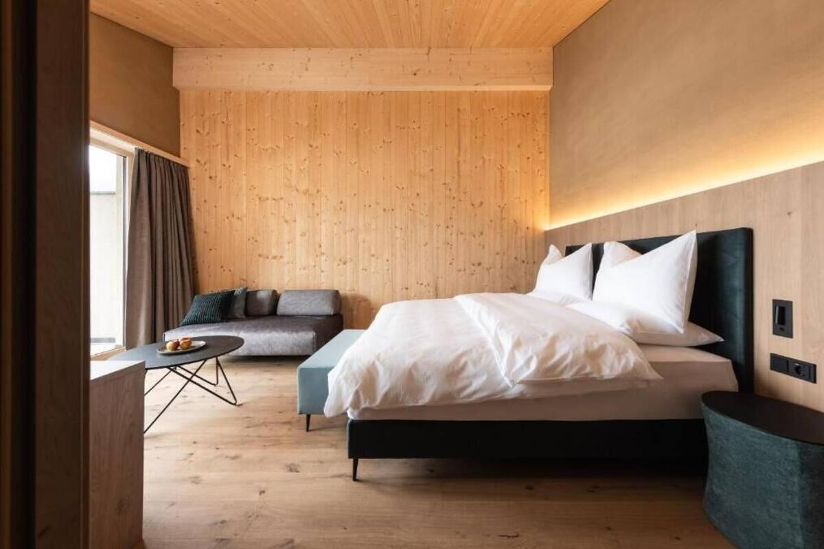 Un dormitorio con cama, sofá, una mesita y ventana con cortinas.