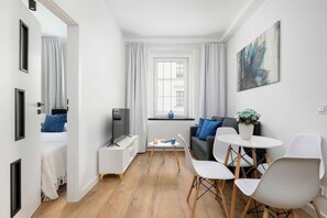 Ein moderner, gut beleuchteter Raum mit einem Bett, einem Fernseher, einem kleinen Tisch mit einer Vase und einem Sofa.