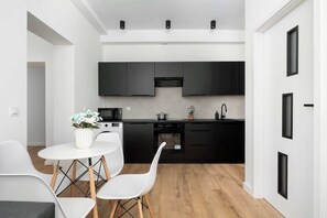 Une cuisine moderne avec des meubles de rangement noirs, une table à manger blanche avec des chaises et une plante en pot posée sur la table.