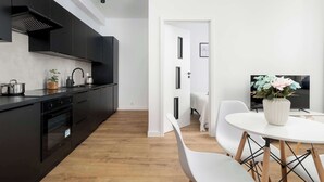 Eine moderne Küche mit schwarzen Schränken, einem weißen Essbereich mit rundem Tisch und einem Fernseher im Hintergrund.