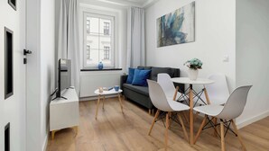 Ein modernes Wohnzimmer mit einer Couch, einem Esstisch mit Stühlen, einem Fernseher und einem Fenster mit Vorhängen.