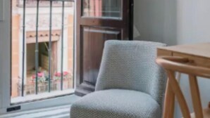 Una habitación con balcón, una silla y una mesa de madera.