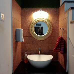 Ein Badezimmer mit einem weißen Waschbecken, einem spiegel mit goldener Rahmen, einem Handseifen-Spender und einem Handtuchhalter mit einem roten Handtuch.