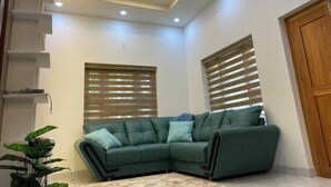 Una sala de estar con un sofá modular, persianas de madera, iluminación empotrada en el techo y un ventilador de techo.