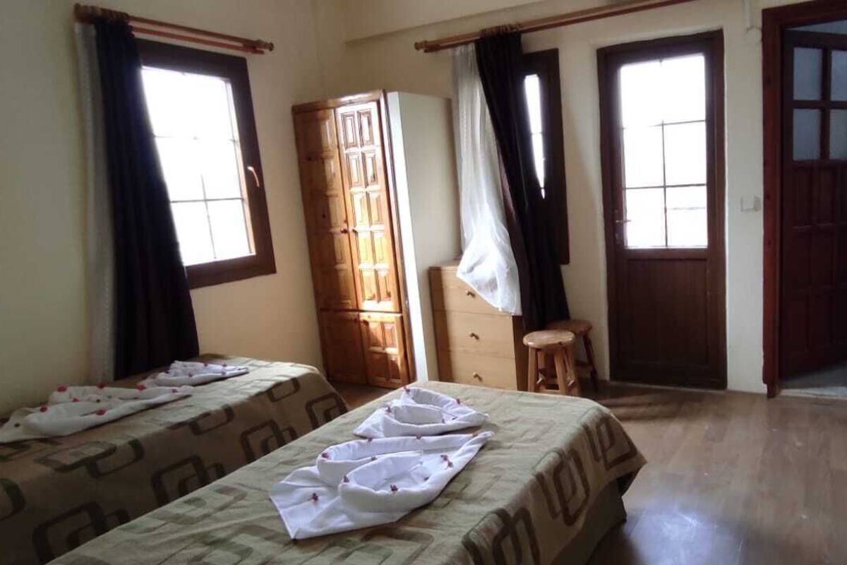 A room with two beds, a wooden wardrobe, a small stool, and a door leading to another room.